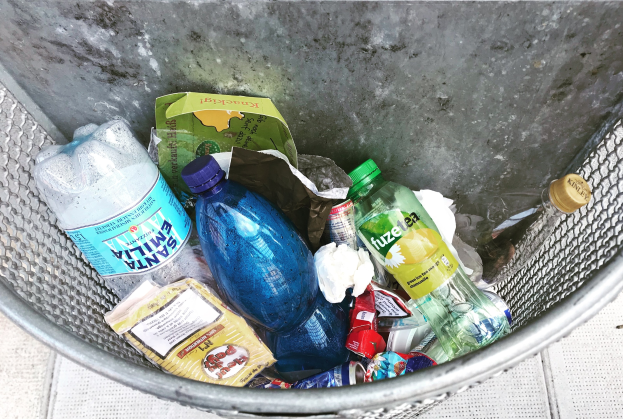 Ein Metallmüllcontainer voller Plastikflaschen, Beutel und anderen Abfällen.