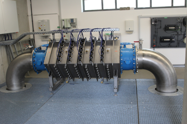 Großer industrieller Wärmetauscher in einem Gebäude mit Fenstern, verbunden durch verschiedene Komponenten und Kabel.