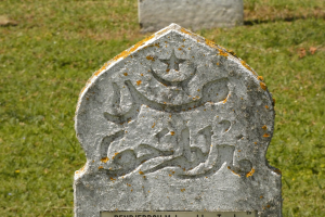 Grabstein mit arabischer Schrift in einem grasbewachsenen Friedhof.