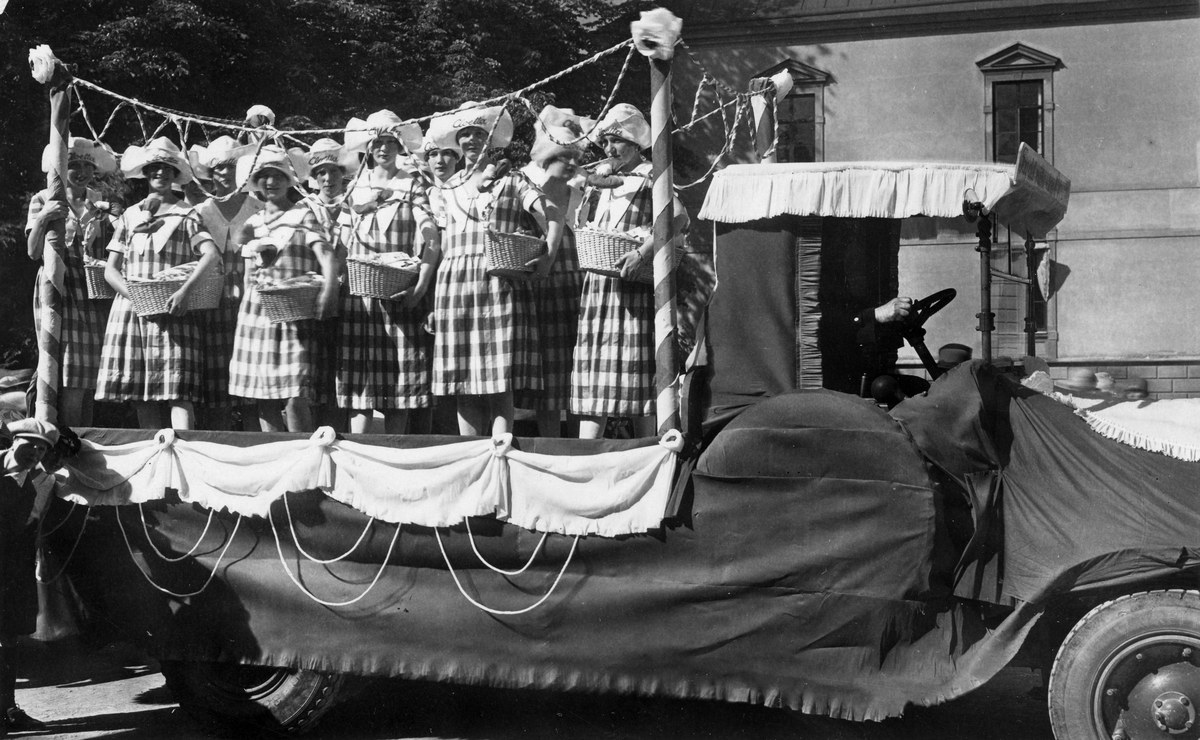 Schwarzes und weißes Foto einer Gruppe von Frauen auf einem Truck, die Körbe halten, mit einem Gebäude und Bäumen im Hintergrund.