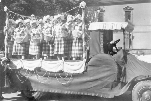 Schwarzes und weißes Foto einer Gruppe von Frauen auf einem Truck, die Körbe halten, mit einem Gebäude und Bäumen im Hintergrund.