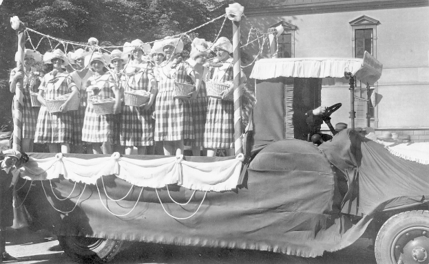 Schwarzes und weißes Foto einer Gruppe von Frauen auf einem Truck, die Körbe halten, mit einem Gebäude und Bäumen im Hintergrund.