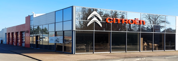 Außenansicht eines Citroën-Autohauses mit Glaswänden und -türen, einer Straße davor und einem klaren blauen Himmel im Hintergrund.