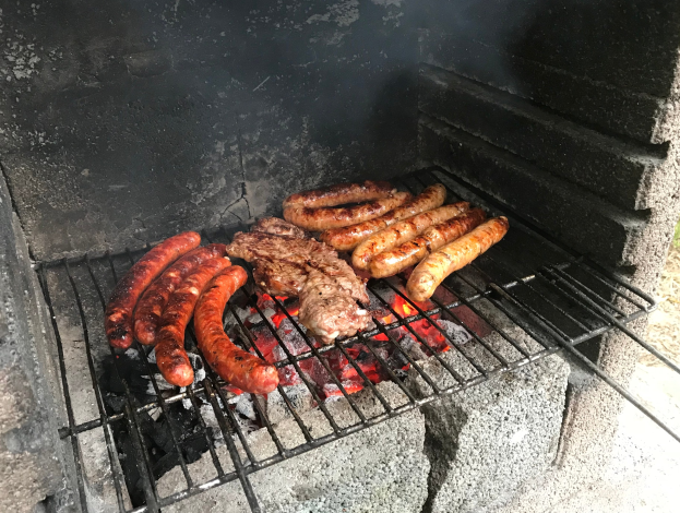Grill mit Würstchen und Fleisch, das über Kohle und Feuer gegrillt wird, auf Gras im Freien
