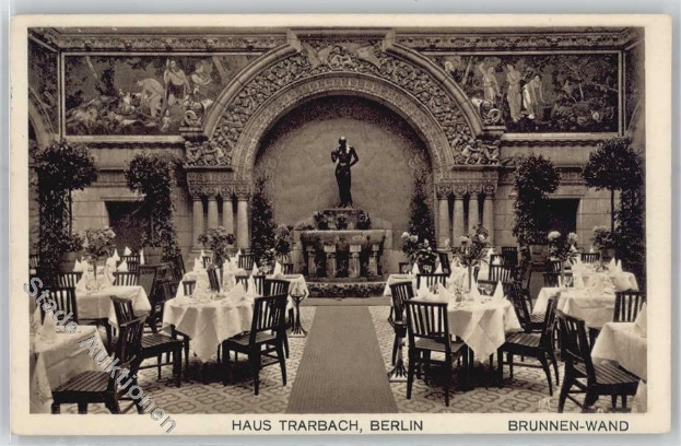 Schwarzes-Weißes-Foto eines alten Berliner Restaurant-Interieurs mit Tischen, Stühlen, Blumenvasen, einer Statue, Wandskulpturen, Pflanzen und Text am Boden.