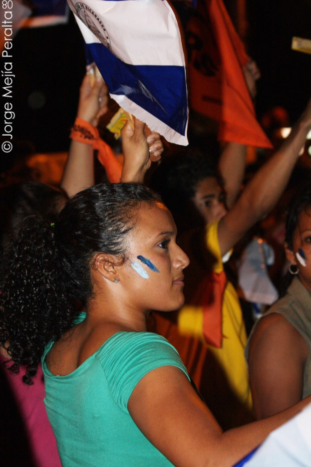 Frauen in grünen T-Shirts halten eine weiße Decke während einer Demonstration, mit mehreren anderen Mädchen, die dahinter stehen.
