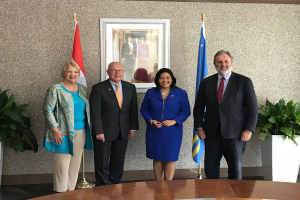 Eine Gruppe strahlender Menschen um einen Tisch mit Papieren stehend, umgeben von Fahnen, Topfpflanzen und einem Foto auf der Wand, feiert die Unterzeichnung eines Memorandums von Verständigung zwischen den Vereinigten Staaten und Kanada.