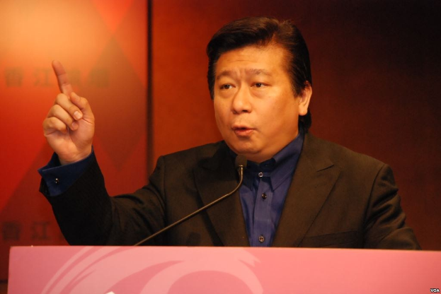 Ein Mann in Anzug und Krawatte, der an einem Rednerpult spricht und dabei ernst wirkt.