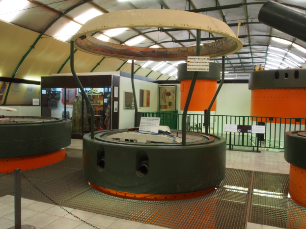 Ein großer Industrieraum mit verschiedenen Maschinen, darunter ein Rotor, Ketten, Stangen, Texttafeln, ein Zaun, Wände, Deckenleuchten und andere Ausrüstung.