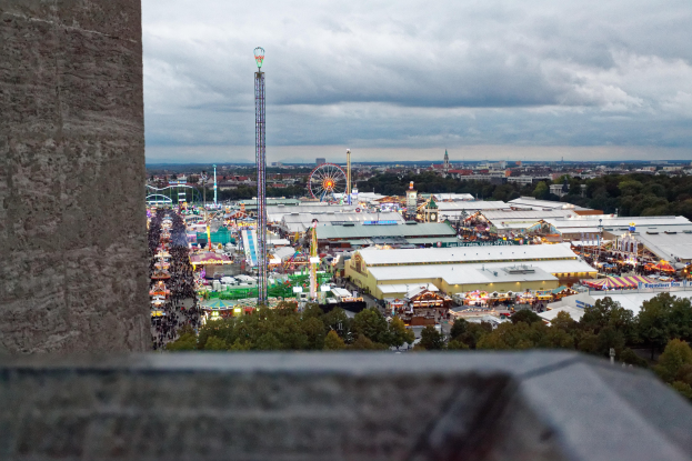 Freizeitpark-Blick von einem Turm aus, mit einer Wand, Bäumen, Gebäuden, Fahrgeschäften, Pfählen und einem bewölkten Himmel im Hintergrund.