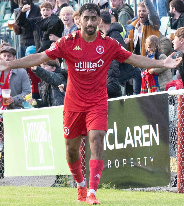 Ein Fußballer in roter Uniform rennt mit ausgestreckten Armen auf einem Feld, mit einer Menge im Hintergrund und einem Banner mit der Aufschrift "Middlesbrough FC vs. Swansea City - Sky Bet Championship" im Vordergrund.