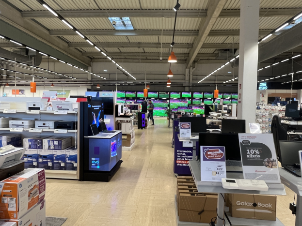 Großer Raum voller Elektronik in Regalen angeordnet, einschließlich Computer und Drucker, mit Menschen auf dem Boden, einer Säule, Schildern, Deckenlampen und Ventilatoren, befindet sich innerhalb eines Walmart-Geschäfts.