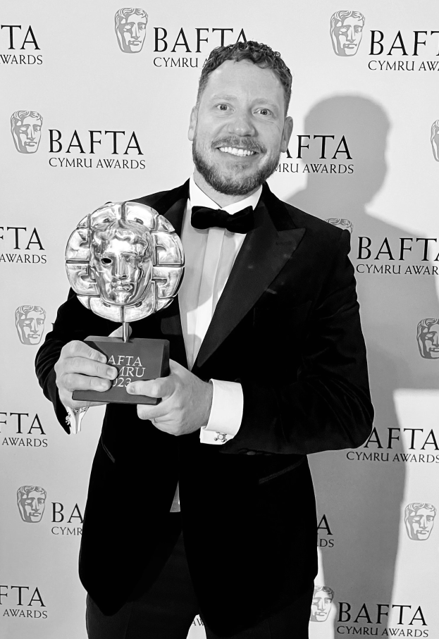 Ein Mann in einem Smoking, der eine BAFTA-Trophäe hält und lächelt, mit einem "BAFTA Awards 2018"-Schild im Hintergrund.