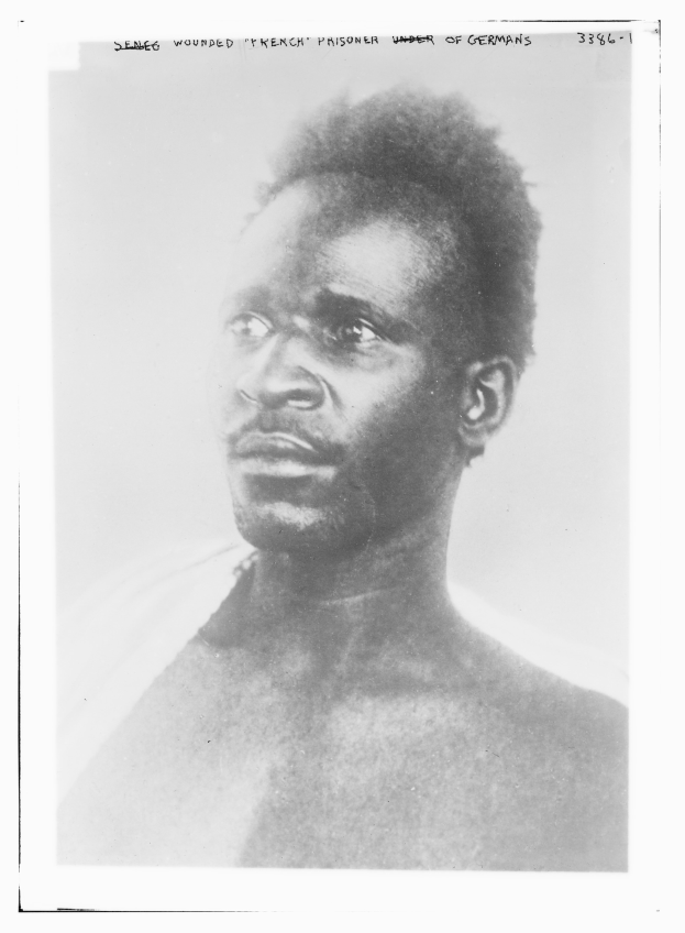 Schwarzes und weißes Foto eines Mannes mit ernstem Gesichtsausdruck, beschriftet mit "Seneg Wounded French Prisoner Under of Germans" oben.