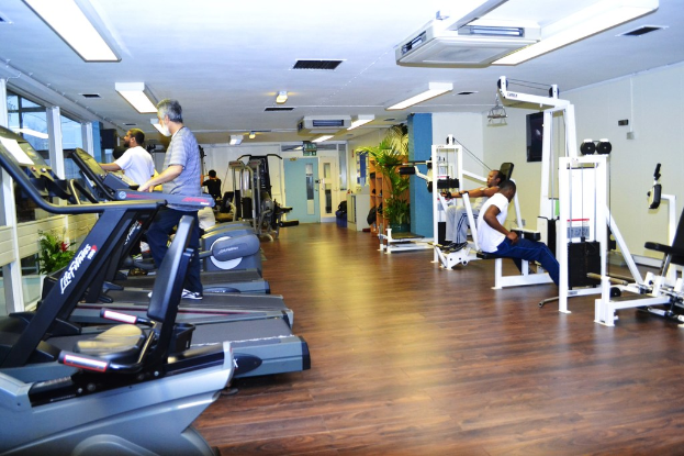 Ein Fitnessstudio mit verschiedenen Trainingsgeräten und Menschen beim Training, mit einer Pflanze auf der rechten Seite.