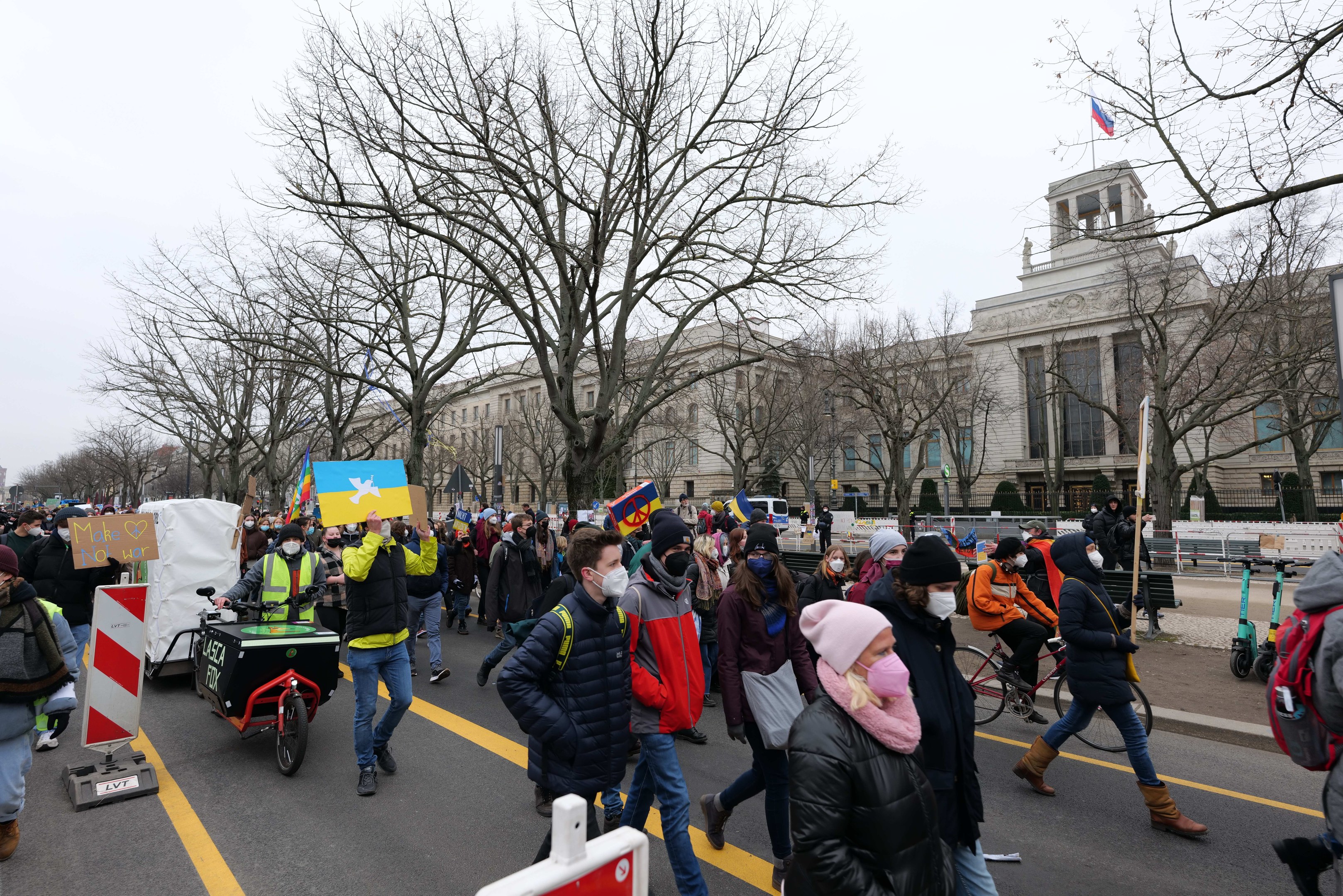 Eine großle Gruppe von Menschen marschiert bei einer Demonstration durch eine Straße in Washington, D.C., mit Schildern und Bannern, während einige Fahrräder fahren, unter einem klaren blauen Himmel.