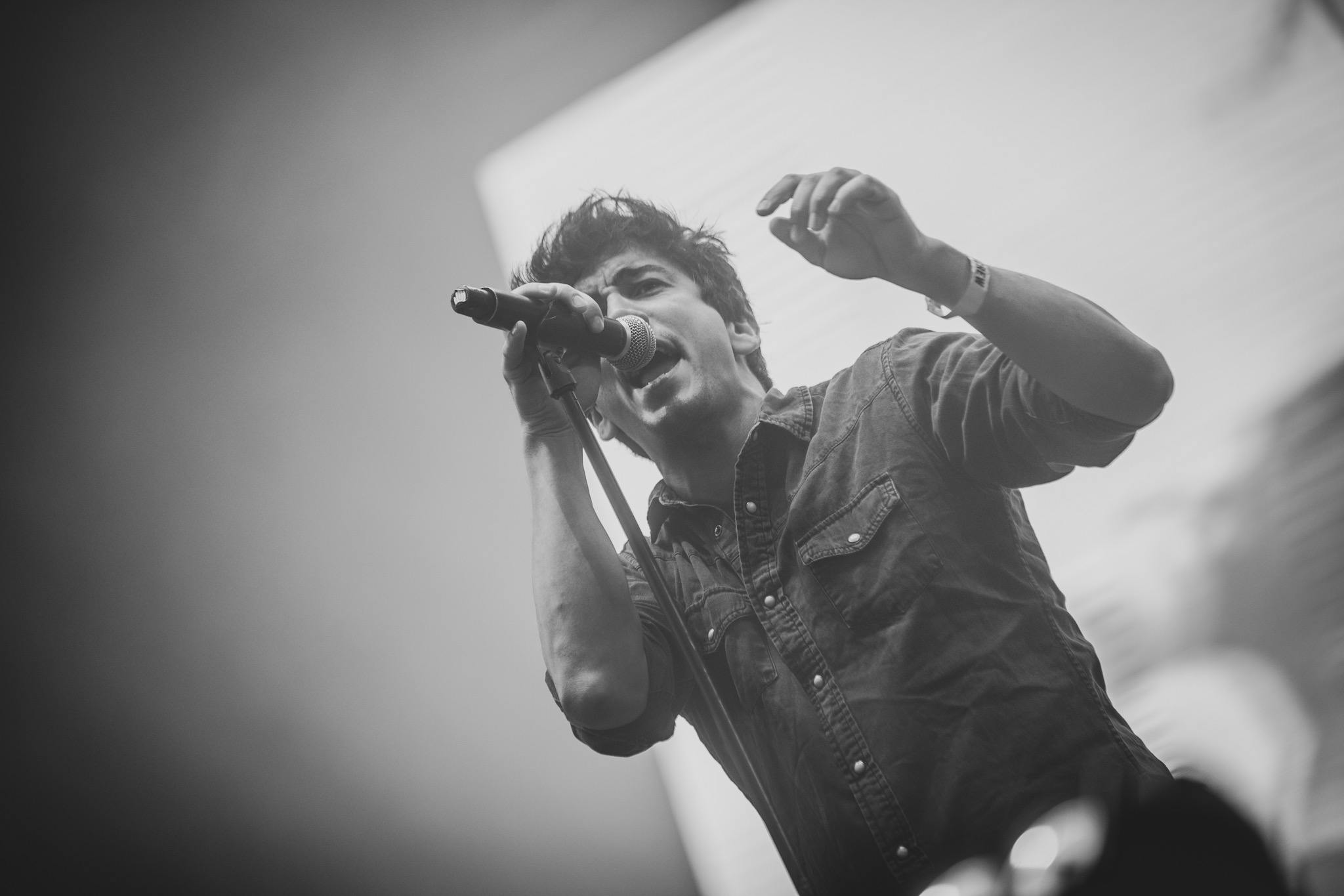 Ein Mann singt in ein Mikrofon auf einem Konzert, mit einem menschlichen Gesicht im Hintergrund, auf einem Schwarz-Weiß-Bild.