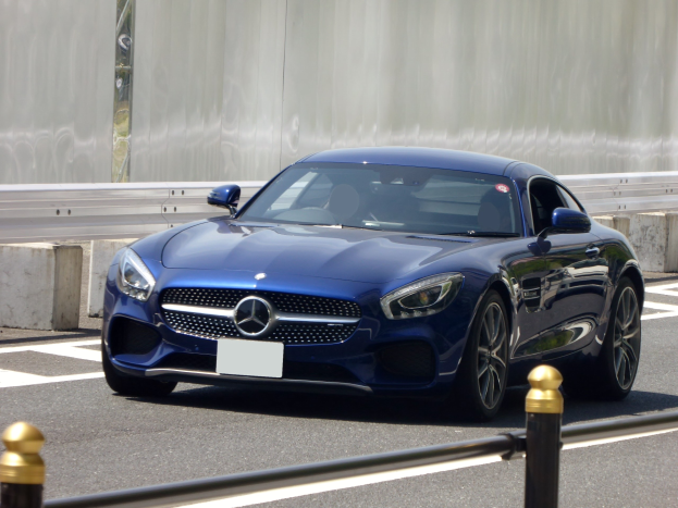 Blauer Mercedes-Benz AMG GT Coupé fährt eine Straße entlang, mit einer Wand im Hintergrund.