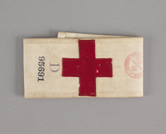 Ein rotes Kreuz-Erste-Hilfe-Set in einer Stofftasche mit Text und einem Stempel, das auf einer Oberfläche liegt.