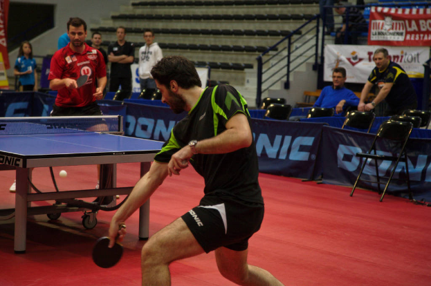 Eine Gruppe von Menschen in verschiedenen Farben, darunter schwarz, wei√ü und blau, versammelt sich um einen Tisch mit einem Spiel im Gange, mit Stühlen und einer Treppe im Hintergrund.