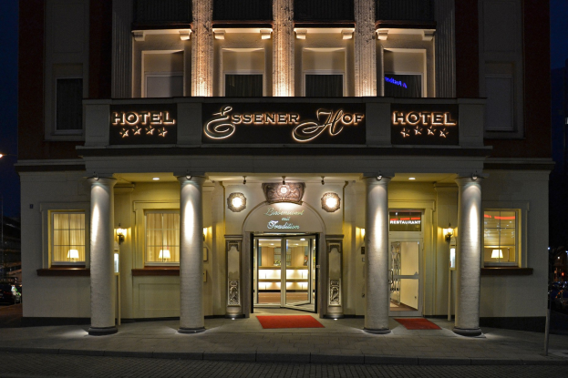 Das Essenerhof Hotel in Berlin, Deutschland, ein mehrstöckiges Gebäude mit Fenstern, Türen, Säulen, Laternen und einem Namensschild, das sichtbar ist, und eine Straße mit Fahrzeugen auf der rechten Seite, unter einem klaren Himmel.