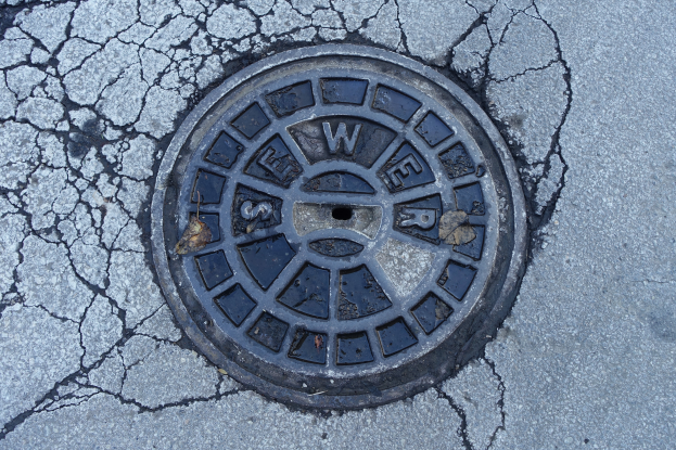Ein Metallgullideckel am Straßenrand mit sichtbaren Rissen und Inschrift.