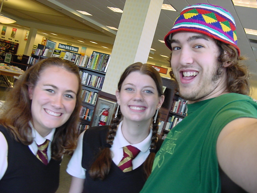 Ein Mann und zwei Schüler machen ein Selfie in einer Bibliothek, im Hintergrund sind Bücherregale mit Büchern gefüllt.