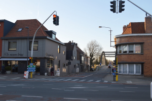 Stadtstraßenkreuzung mit Ampel, Fußgängern, Fahrrädern, Gebäuden, Bäumen, Schildern, Laternen und einem Bogen.