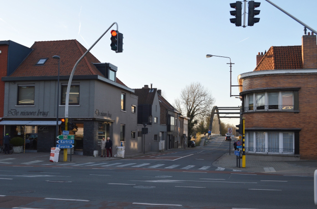 Stadtstraßenkreuzung mit Ampel, Fußgängern, Fahrrädern, Gebäuden, Bäumen, Schildern, Laternen und einem Bogen.