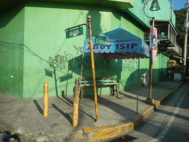 Grünes Bauen mit Graffiti, einem blauen Zelt, einer Bank, Pfosten, Lampen, Plakaten, einem Fahrrad, Bäumen und anderen Gegenständen im Vordergrund vor einem Himmelhintergrund.