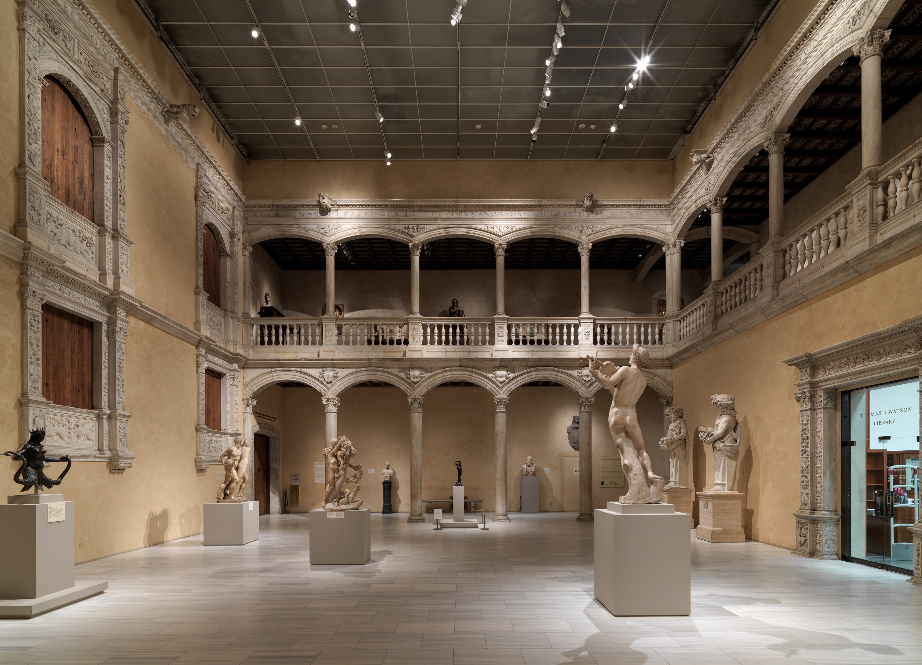Große Museumsgalerie mit zahlreichen Statuen und Skulpturen auf Sockeln, architektonischen Elementen wie Wänden, Säulen und Geländern, Deckenbeleuchtung und wenigen Besuchern.