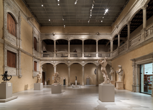 Große Museumsgalerie mit zahlreichen Statuen und Skulpturen auf Sockeln, architektonischen Elementen wie Wänden, Säulen und Geländern, Deckenbeleuchtung und wenigen Besuchern.