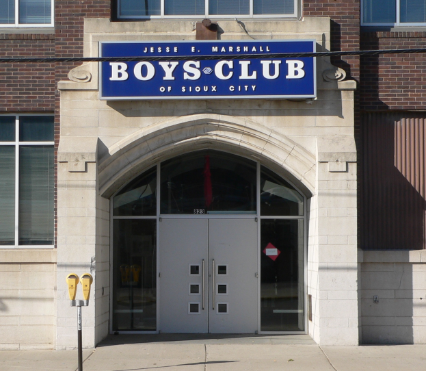 Das Gebäude des Boys Club von Sioux City mit Glasfenstern und -türen, einer Schautafel mit Text und einem Pfahl auf dem angrenzenden Gehweg.