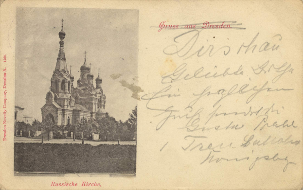 Eine Schwarz-Weiß-Postkarte mit dem Bild der Erlöserkirche auf dem Blutsfeld in Dresden, umgeben von Bäumen unter einem klaren blauen Himmel, mit deutschem Text auf der rechten Seite.