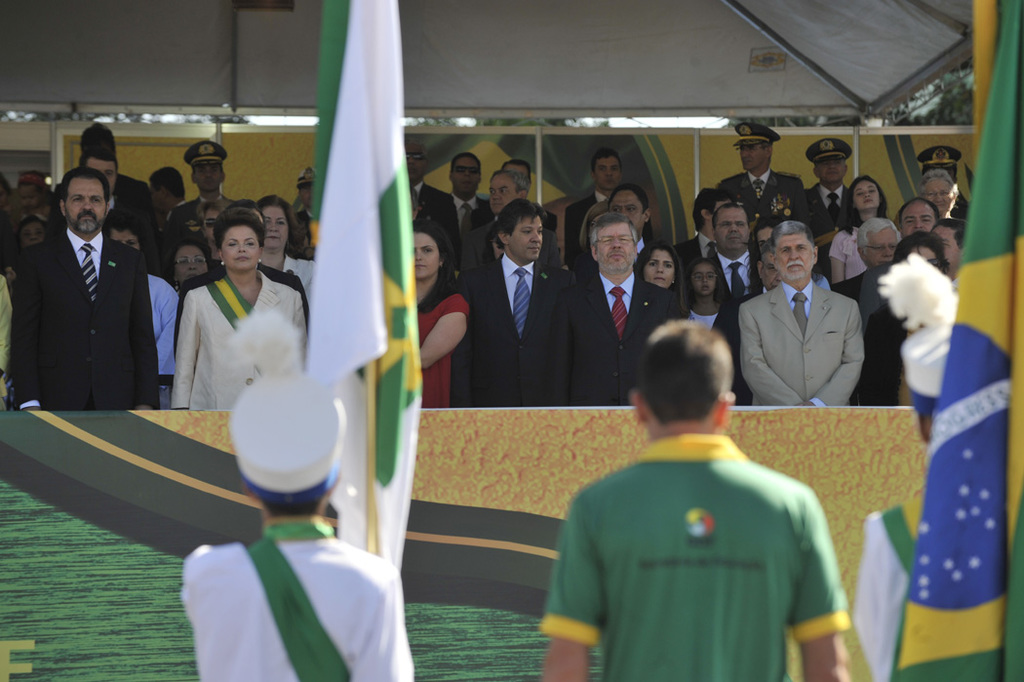 Menschen bei Flaggen, mit einem Banner im Hintergrund und mehr Menschen unter einem Zelt.