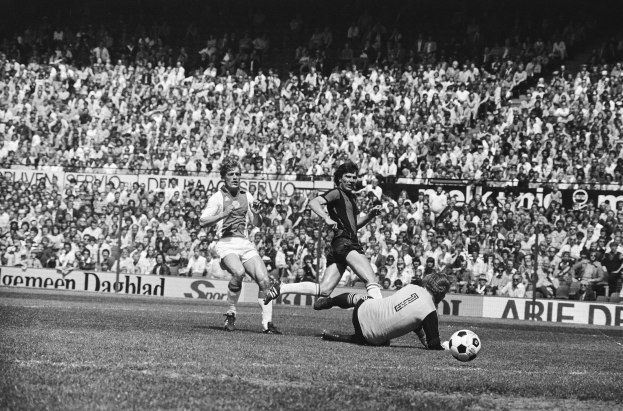 Schwarze-weiß-Fotografie von Männern beim Fußballspielen auf einem Feld mit Zuschauern im Hintergrund und einer "Bundesliga 1978-79 Ajax 1-1 Hannover 96"-Tafel.