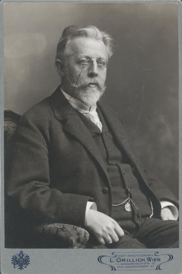 Schwarz-weiß-Porträt eines bärtigen Mannes in Brille, der in einem Stuhl sitzt, mit Text unten, der ihn als L. Grillich Wien, den Gründer der deutschen Revolution identifiziert.