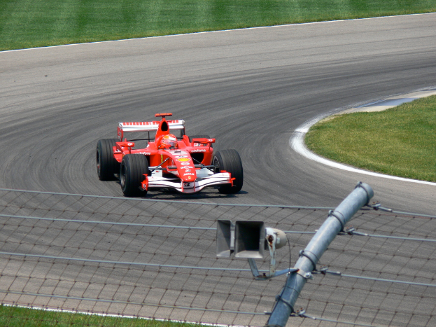 Ein Fahrzeug fährt auf einer von Gras und einem Maschendrahtzaun umgebenen Straße.