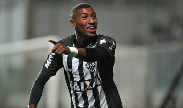 Ein Fußballspieler in einem schwarz-weißen gestreiften Trikot lächelt beim Feiern eines Tores mit einem unscharfen Hintergrund.