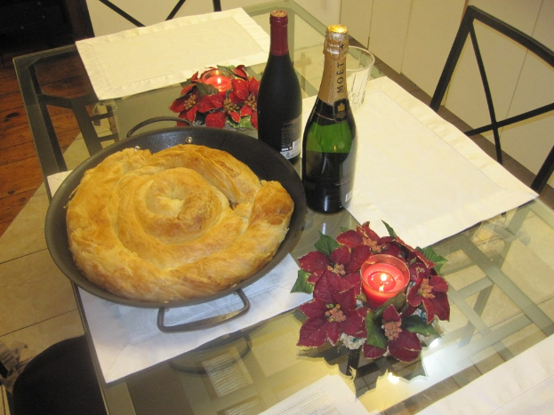 Ein Tisch mit Weinflaschen, Kerzen, Gläsern, einer Blumenvase und einer Schüssel mit Essen, mit Stühlen und einer Wand im Hintergrund.
