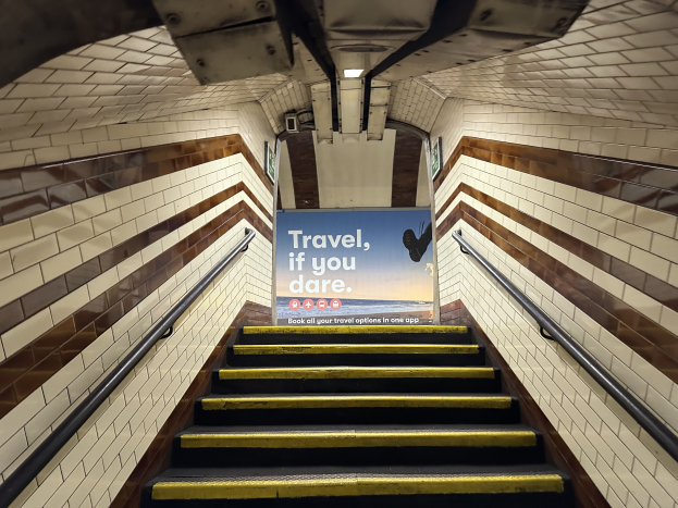 Eine Treppe in einer U-Bahn-Station mit einem 'Reise, wenn du wagst'-Schild oben, flankiert von Geländern und Stationswänden im Hintergrund.