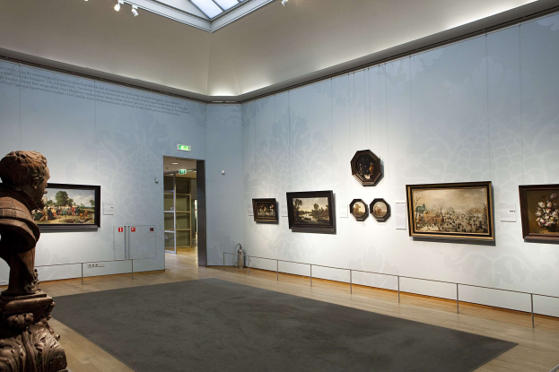 Ein prächtiger Raum im Kunsthistorischen Museum in München, Deutschland, mit einer Statue links, einem Teppichboden, Fotorahmen an den Wänden, einer Glasdecke mit Lampen und Türen im Hintergrund.