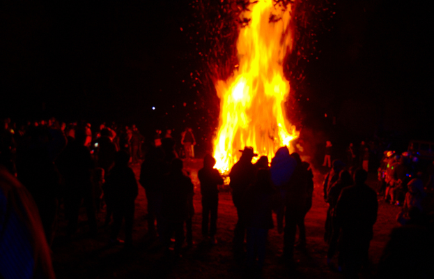 Eine Gruppe von Menschen steht vor einem Feuer im Hintergrund.