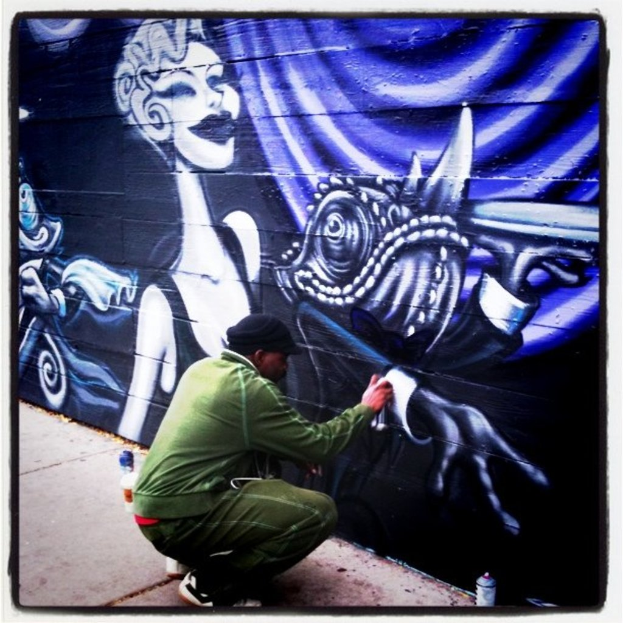 Eine Person mit einer Flasche in der Hand und anderen Flaschen auf der Straße, Graffiti an einer Wand im Hintergrund.