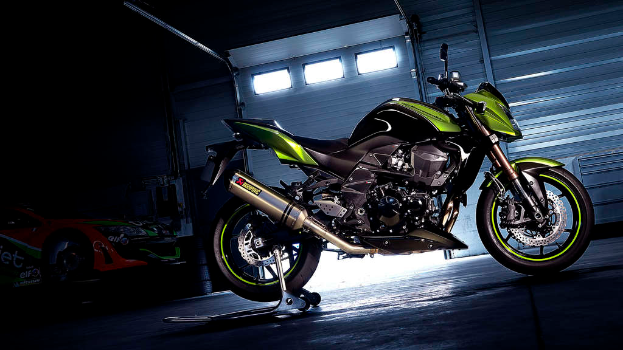 Ein grünes und schwarzes Fahrzeug ist in der Mitte des Bildes zu sehen, mit einem Auto links und einer Klappe im Hintergrund.