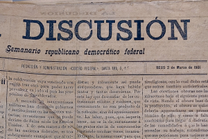Ein vergilbtes, leicht zerknittertes Zeitungsblatt mit der schwarzen Schrift "Diskussion", das die Überschrift "Semanario Repúblicano Democrático Federal" trägt.