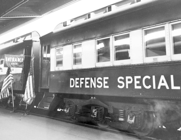 Schwarz-weiß-Foto eines Zuges mit der Aufschrift "Defense Special" auf den Gleisen mit zwei Fahnen links und einer Decke oben.