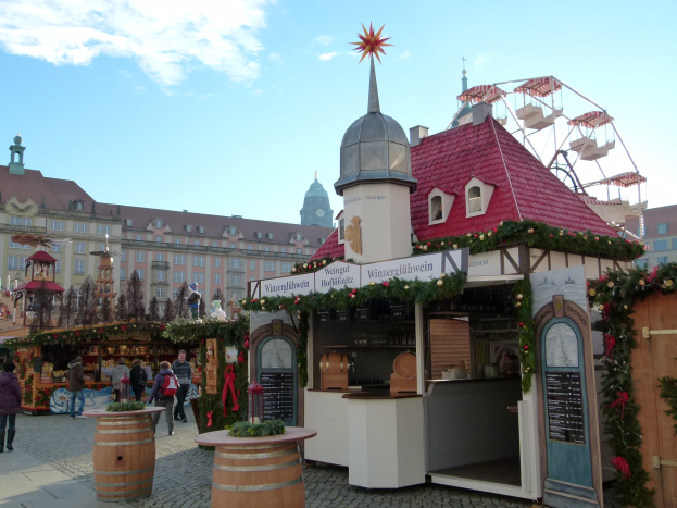 Ein geschäftiger Weihnachtsmarkt in Nürnberg, Deutschland, mit Menschen um geschmückte Stände, festliche Lichter, Schmuck, Gebäude mit Fenstern, ein großes Rad und einen bewölkten Himmel, mit einer Tafel mit Text auf der rechten Seite.