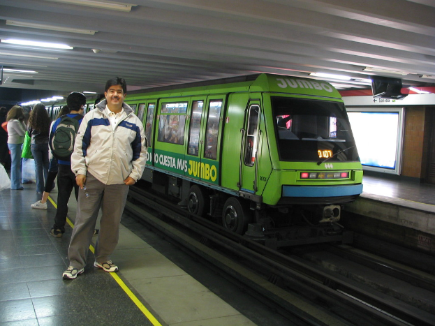 Ein Zug auf Schienen mit Menschen, die links stehen und ein Dach an der Spitze des Bildes.